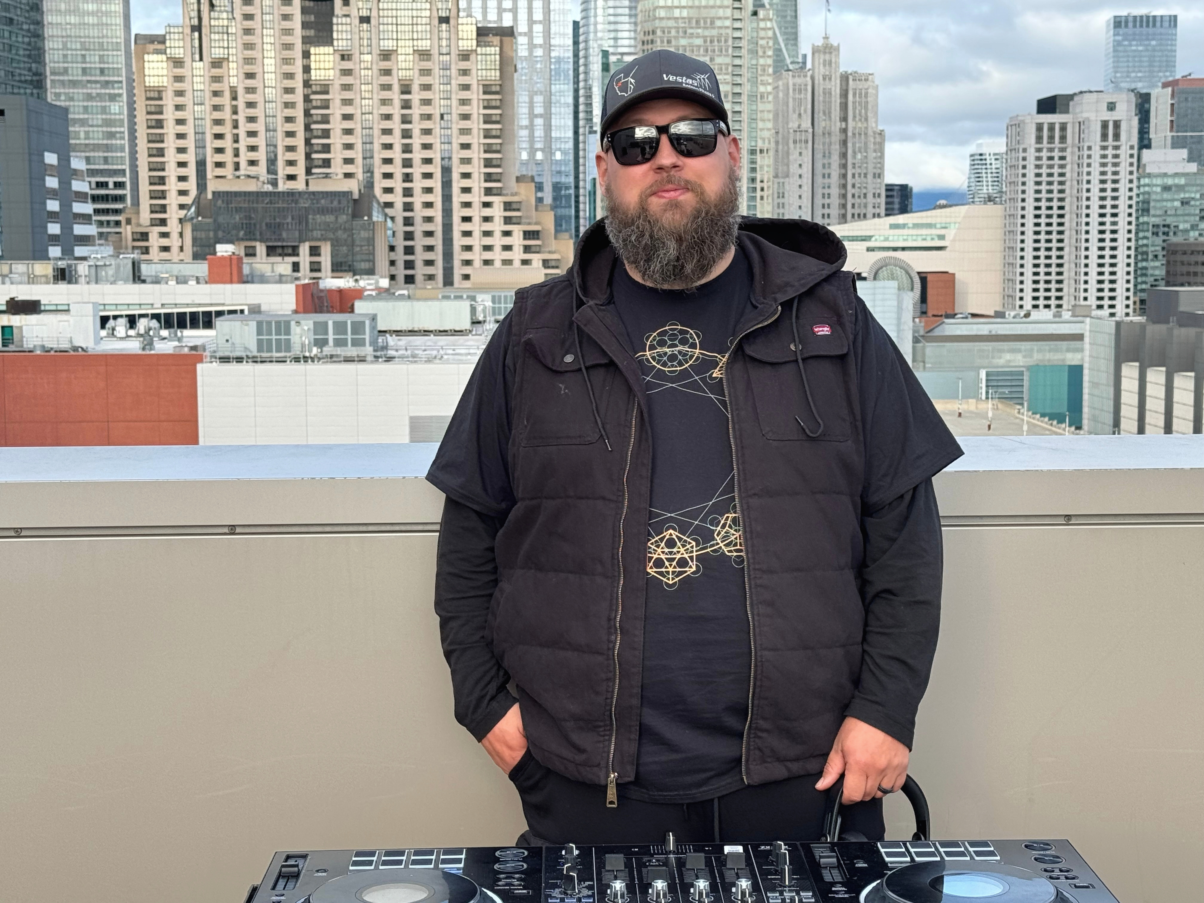 Travis Barnes standing behind a DJ controller with a city skyline in the background